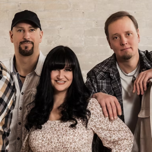 Five people pose together against a light brick wall, smiling at the camera.