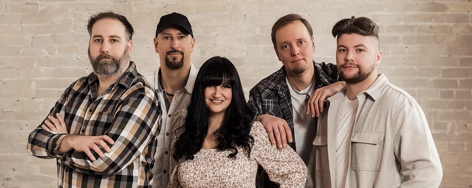 Five people pose together against a light brick wall, smiling at the camera.