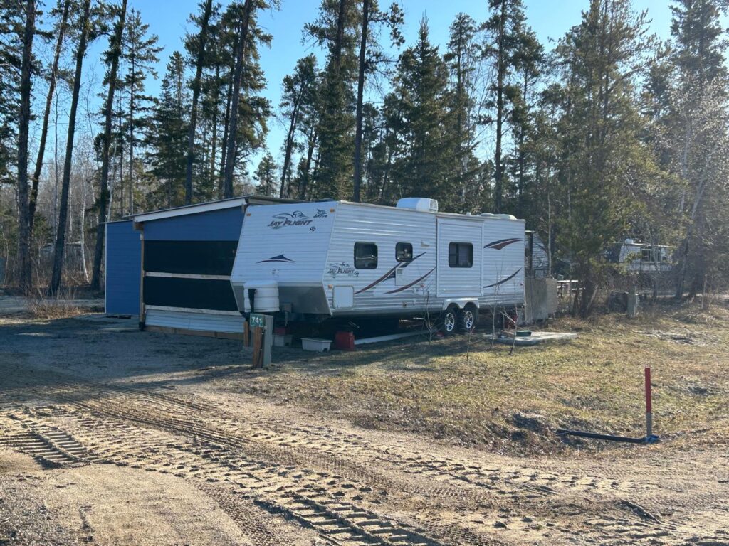 White Jay Flight travel trailer parked beside a blue shed in a wooded campground.